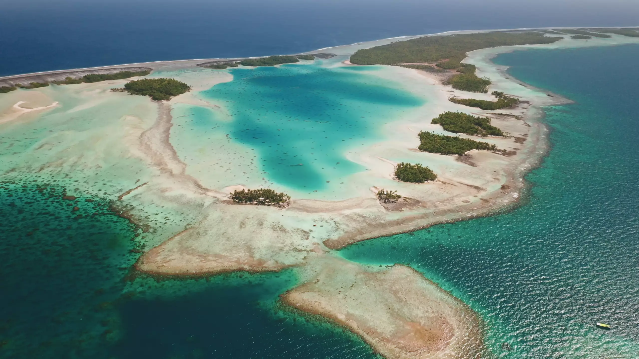 Luftaufnahme eines Korallenatolls der Tuamotu-Inseln mit türkisfarbener Lagune, kleinen Palmeninseln und weißen Sandbänken.